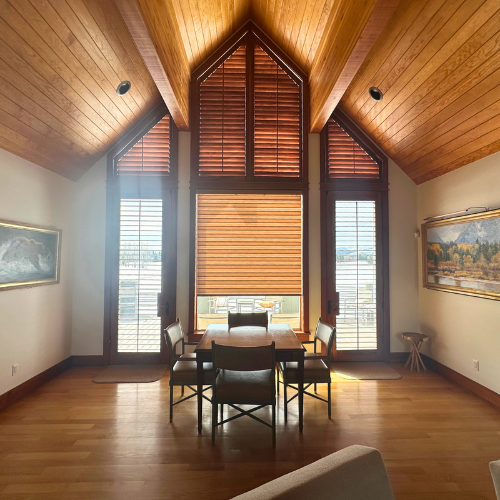 Window covering in dining room with table and paintings around